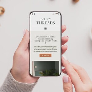 Puede incluir: Un tel&eacute;fono inteligente muestra el sitio web "GOLDEN THREADS" con el texto "&iquest;Est&aacute;s listo para construir una estrategia de marketing de contenidos que realmente funcione?" El tel&eacute;fono lo sostiene una persona.