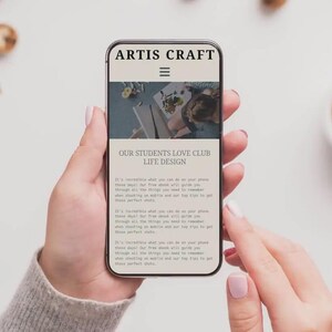 Puede incluir: Un smartphone muestra el sitio web "ARTIS CRAFT" y "OUR STUDENTS LOVE CLUB LIFE DESIGN". El tel&eacute;fono lo sostiene una persona. Una taza de caf&eacute; y galletas est&aacute;n en el fondo.