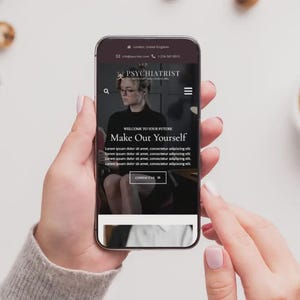 May include: A smartphone displays a website for a psychiatrist, with the text "Make Out Yourself." The phone is held by a person with a neutral background, alongside a cup of coffee and cookies.