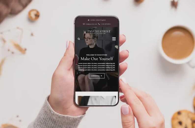May include: A smartphone displays a website for a psychiatrist, with the text "Make Out Yourself." The phone is held by a person with a neutral background, alongside a cup of coffee and cookies.