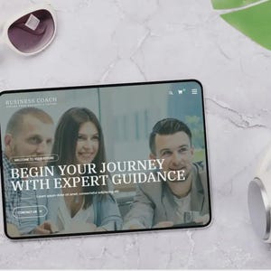 May include: A tablet showing a website with the text "BUSINESS COACH" and "BEGIN YOUR JOURNEY WITH EXPERT GUIDANCE." The image also includes white sunglasses, white headphones, and a green leaf on a marble surface.