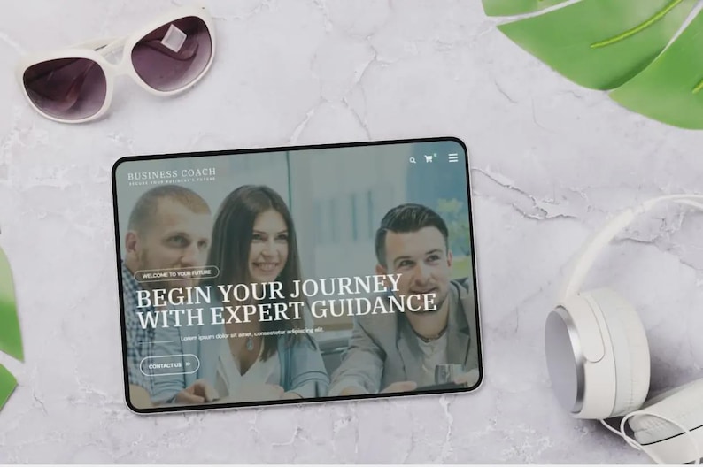 May include: A tablet showing a website with the text "BUSINESS COACH" and "BEGIN YOUR JOURNEY WITH EXPERT GUIDANCE." The image also includes white sunglasses, white headphones, and a green leaf on a marble surface.
