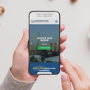 May include: A smartphone screen shows a construction company website with the words "SERVICE AND REPAIR" and a phone number. The phone is held by a person. A cup of coffee and biscuits are in the background.