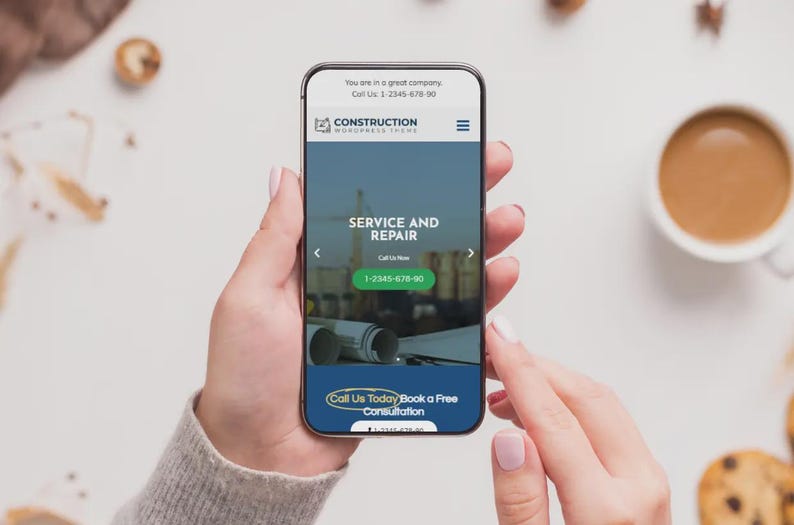 May include: A smartphone screen shows a construction company website with the words "SERVICE AND REPAIR" and a phone number. The phone is held by a person. A cup of coffee and biscuits are in the background.