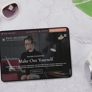 May include: A tablet displaying a website for a psychiatrist, with the text "Make Out Yourself." White sunglasses and headphones are next to the tablet. The website features a woman wearing glasses. The background is a marble surface.