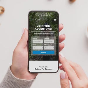 May include: A smartphone screen shows a hiking website with the text "Join the Adventure!". The phone displays a search form and a phone number. The phone is held by a person, with a cup of coffee and biscuits in the background.