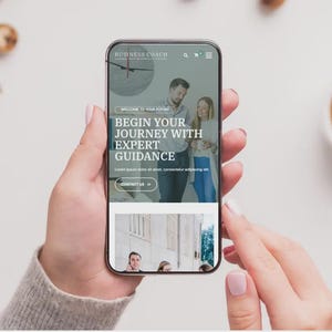 May include: A smartphone screen shows a website with the text "BEGIN YOUR JOURNEY WITH EXPERT GUIDANCE." The phone is held by a person. A cup of coffee and biscuits are in the background.