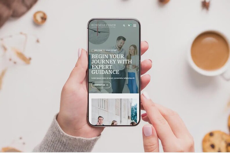 May include: A smartphone screen shows a website with the text "BEGIN YOUR JOURNEY WITH EXPERT GUIDANCE." The phone is held by a person. A cup of coffee and biscuits are in the background.