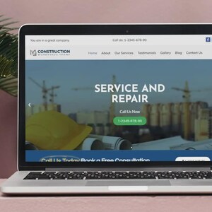 May include: A laptop screen shows a construction company website. The site has a blue and white design, displaying "SERVICE AND REPAIR" and a call to action button. A yellow hard hat is also visible on the screen.