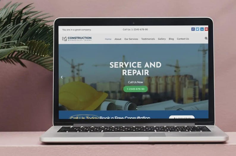 May include: A laptop screen shows a construction company website. The site has a blue and white design, displaying "SERVICE AND REPAIR" and a call to action button. A yellow hard hat is also visible on the screen.