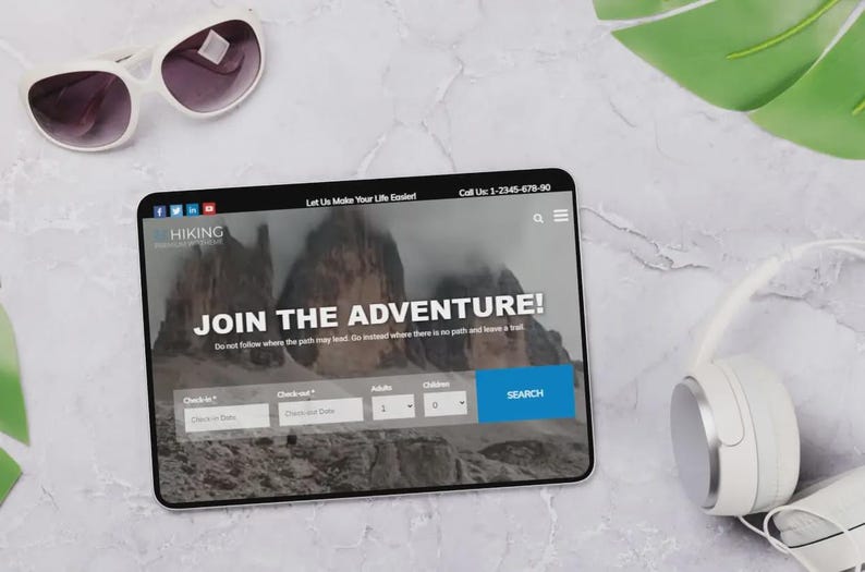 May include: A tablet showing a hiking website with the words "JOIN THE ADVENTURE!". White sunglasses and headphones are placed beside the tablet. The website includes a search function. The background is a marble surface.