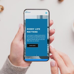 Puede incluir: Un tel&eacute;fono inteligente muestra un sitio web con el texto "EVERY LIFE MATTERS" en blanco sobre un fondo azul. El tel&eacute;fono lo sostiene una persona. Una taza de caf&eacute; y galletas se ven en el fondo sobre una superficie blanca.