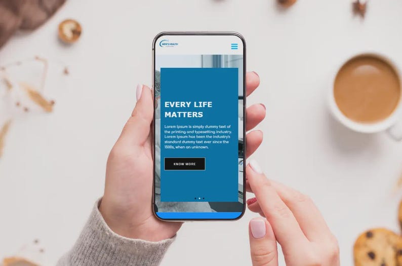 Puede incluir: Un tel&eacute;fono inteligente muestra un sitio web con el texto "EVERY LIFE MATTERS" en blanco sobre un fondo azul. El tel&eacute;fono lo sostiene una persona. Una taza de caf&eacute; y galletas se ven en el fondo sobre una superficie blanca.