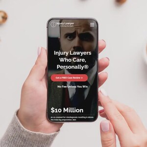 May include: A smartphone displays a website for Injury Lawyers. The screen features the text "Injury Lawyers Who Care, Personally&reg;" with a red button that says "Get a FREE Case Review." The phone is held by a person, with a cup of coffee and cookies in the background.