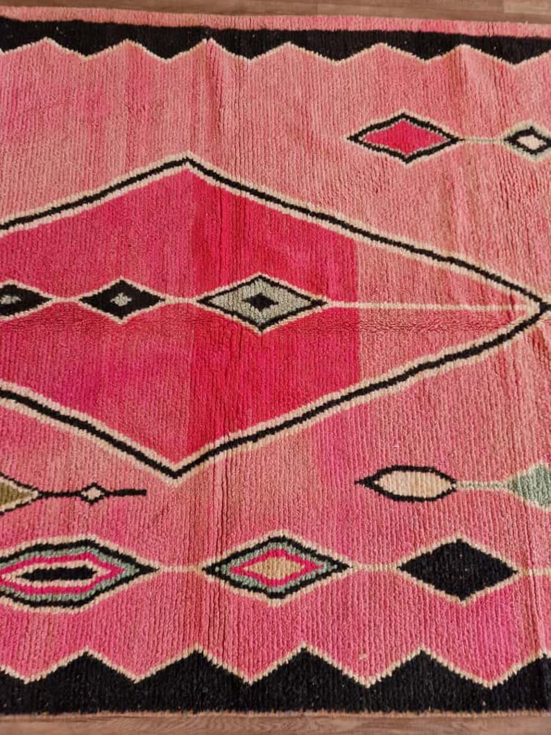 May include: A pink and black geometric rug with a diamond pattern. The rug features a gradient of pink hues, from light to dark, with black zigzag borders and diamond shapes in various colors.