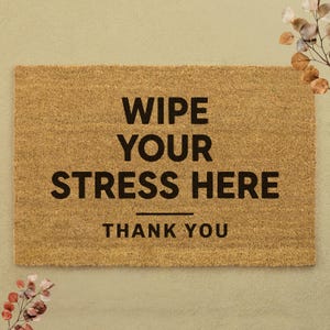 May include: A rectangular doormat made of natural brown coir fiber. The mat features the text "WIPE YOUR STRESS HERE" in bold black letters, with "THANK YOU" below. Decorative floral elements are in the corners.