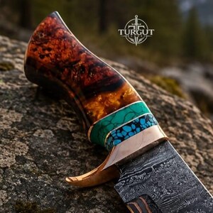 May include: A fixed-blade knife featuring a polished Damascus steel blade and a handle crafted from dark brown burl wood. The handle includes decorative bands of turquoise and blue stone inlays, accented by a metallic bolster with a curved guard.