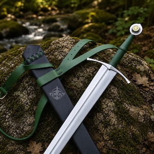 Può includere: Una spada in acciaio con impugnatura verde e guardia in argento, dotata di un pomolo con un emblema circolare dorato. È accompagnata da un fodero nero contrassegnato dal logo Turgut e da una cinghia in pelle verde per trasportare l'arma.