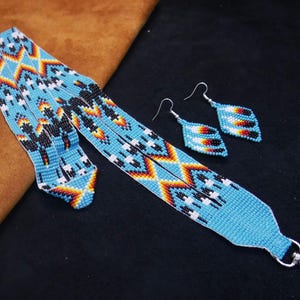 May include: A beaded lanyard and matching earrings set. The lanyard and earrings are light blue with a geometric pattern in black, white, orange, and yellow. The earrings are diamond-shaped with silver hooks. The lanyard has a silver clasp.