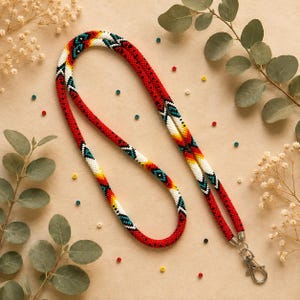 May include: A beaded lanyard featuring a vibrant geometric pattern in red, white, yellow, and teal. The tubular cord is constructed from small glass beads and terminates in a silver-toned metal swivel lobster clasp for attaching items.