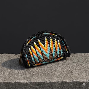 Op de afbeelding: Een zwarte, met kralen bezette portemonnee met een kleurrijk geometrisch ontwerp. De portemonnee heeft een ritssluiting en een halve maanvorm. Het kralenpatroon bevat oranje, gele, blauwe en witte kralen.