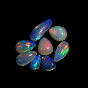 May include: A collection of eight polished, teardrop-shaped opals arranged in a cluster. Each gemstone features a translucent, milky white base with vibrant flashes of iridescent colour, including bright green, orange, and blue, against a black background.