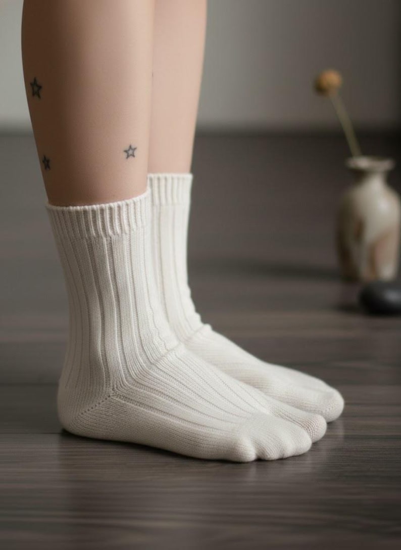 Puede incluir: Un par de calcetines acanalados de color crema. Los calcetines est&aacute;n hechos de un material suave y tienen un dise&ntilde;o cl&aacute;sico. Los calcetines se muestran en las piernas de una persona. El fondo est&aacute; borroso, con un jarr&oacute;n y un suelo de madera oscura.