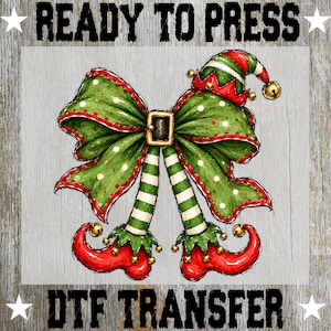 May include: A DTF transfer featuring a green bow with red trim, a gold buckle, and elf legs with green and white striped stockings and curled red shoes with gold bells. The text READY TO PRESS DTF TRANSFER is included.