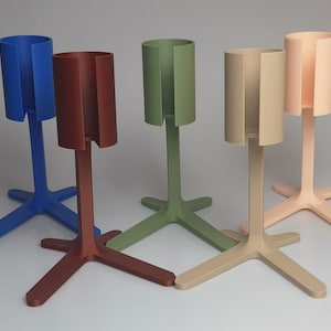May include: Five vertical stands with a cylindrical top featuring a vertical slit opening. The stands are colored in blue, dark red, olive green, beige, and light peach. Each stand has a tripod-style base for stability on a flat surface.