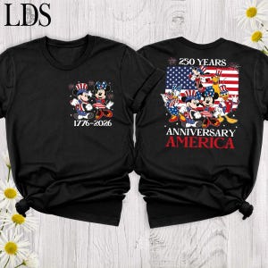 May include: A black t-shirt featuring a front graphic of Mickey and Minnie Mouse in patriotic attire with the text 1776-2026. The back displays a large American flag with Disney characters, the text 250 YEARS ANNIVERSARY AMERICA, and fireworks.