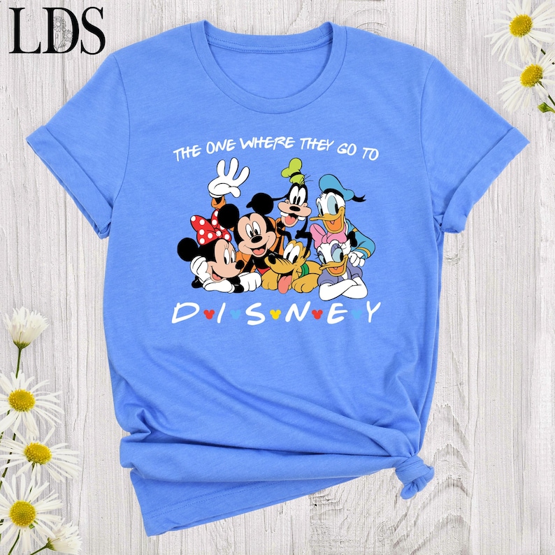 Puede incluir: Camiseta azul claro con un gr&aacute;fico de personajes de Disney, incluyendo Mickey y Minnie Mouse, Goofy, Donald y Daisy Duck, y Pluto. El texto en la camiseta dice "THE ONE WHERE THEY GO TO DISNEY".