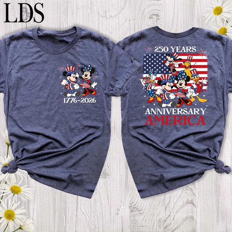 May include: A heathered navy blue t-shirt featuring a small graphic on the front with Mickey and Minnie Mouse in patriotic attire and the text 1776-2026. The back displays a large American flag graphic with Disney characters and the text 250 YEARS ANNIVERSARY AMERICA.