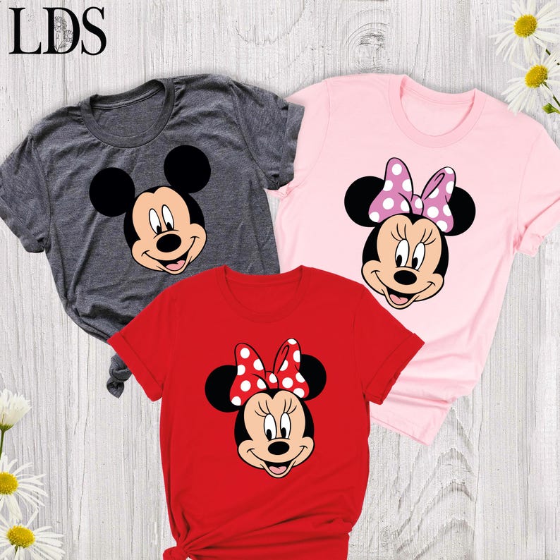May include: Three t-shirts featuring cartoon characters. A gray t-shirt with Mickey Mouse's face, a pink t-shirt with Minnie Mouse wearing a polka dot bow, and a red t-shirt with Minnie Mouse wearing a polka dot bow. The letters "LDS" are in the top left corner.