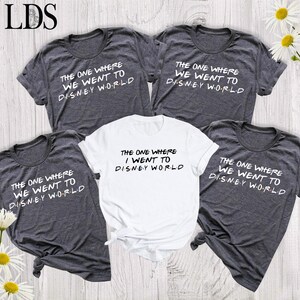 May include: Four short-sleeved t-shirts, three in dark heather gray and one in white, each featuring the black text "THE ONE WHERE WE WENT TO DISNEY WORLD" or "THE ONE WHERE I WENT TO DISNEY WORLD" with colorful dots between the letters of Disney World.