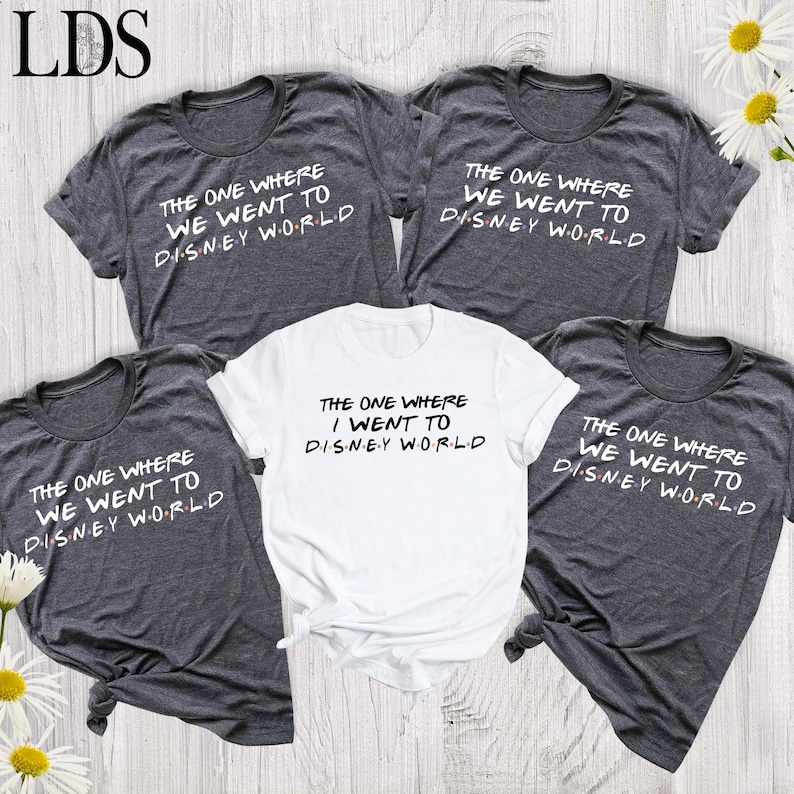 May include: Four short-sleeved t-shirts, three in dark heather gray and one in white, each featuring the black text "THE ONE WHERE WE WENT TO DISNEY WORLD" or "THE ONE WHERE I WENT TO DISNEY WORLD" with colorful dots between the letters of Disney World.