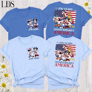 May include: Two blue t-shirts featuring Mickey and Minnie Mouse in patriotic outfits. The front shows the characters with the text 1776-2026. The back displays the characters with an American flag, the text 250 YEARS ANNIVERSARY AMERICA, and fireworks.