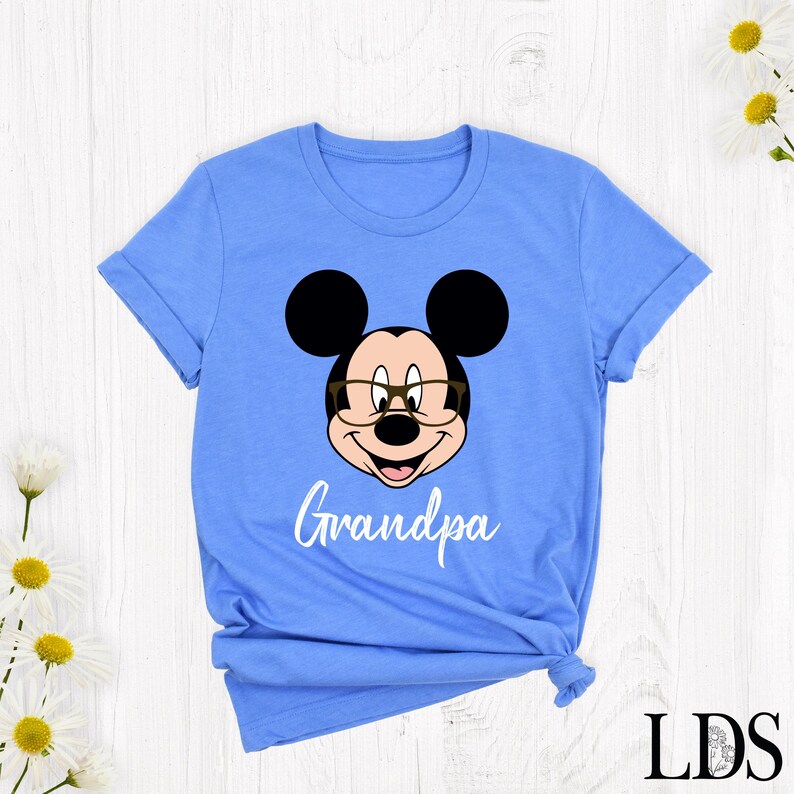 Puede incluir: Camiseta azul claro con la cara de un rat&oacute;n de dibujos animados con gafas y la palabra "Grandpa" en escritura blanca. El rat&oacute;n tiene orejas negras y una cara sonriente. La camiseta es de cuello redondo.
