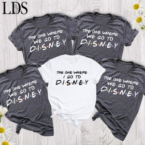 May include: Three dark heather gray t-shirts and one white t-shirt. The dark gray shirts feature the white text "THE ONE WHERE WE GO TO DISNEY" with colorful dots between the letters. The white shirt features the text "THE ONE WHERE I GO TO DISNEY".