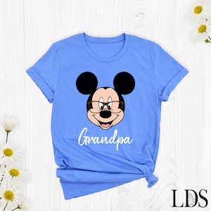 Puede incluir: Camiseta azul claro con la cara de un rat&oacute;n de dibujos animados con gafas y la palabra "Grandpa" en escritura blanca. El rat&oacute;n tiene orejas negras y una cara sonriente. La camiseta es de cuello redondo.