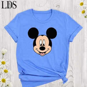 May include: A light blue t-shirt featuring a large graphic of Mickey Mouse's face. The cartoon character's black ears, smiling face, and the text "LDS" at the top left corner are visible. The shirt has short sleeves and a tied knot at the bottom.