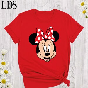 May include: Red t-shirt featuring a graphic of Minnie Mouse's face. The cartoon character has a red and white polka dot bow, black ears, and a smiling expression. The letters "LDS" are in the top left corner.