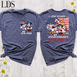 May include: A heathered navy blue t-shirt featuring a small graphic on the front with Mickey and Minnie Mouse in patriotic attire and the text 1776-2026. The back displays a large American flag graphic with Disney characters and the text 250 YEARS ANNIVERSARY AMERICA.