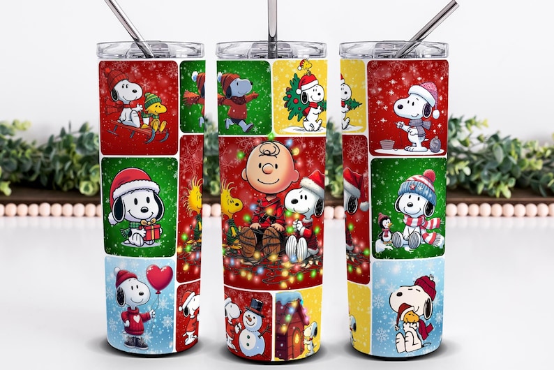 May include: A stainless steel tumbler featuring a festive design with Snoopy and Woodstock in various Christmas scenes. The tumbler has a red, green, and yellow color scheme with a silver straw and lid. The design includes snowflakes and holiday elements.