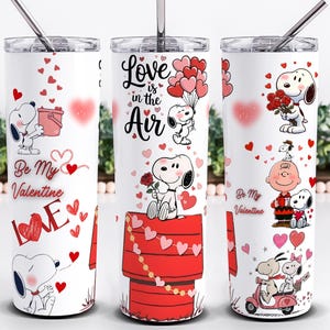 May include: White stainless steel tumbler featuring Snoopy and Woodstock Valentine's Day designs. The tumbler has a silver straw and lid. The designs include Snoopy with hearts, roses, and the text "Love is in the Air" and "Be My Valentine".