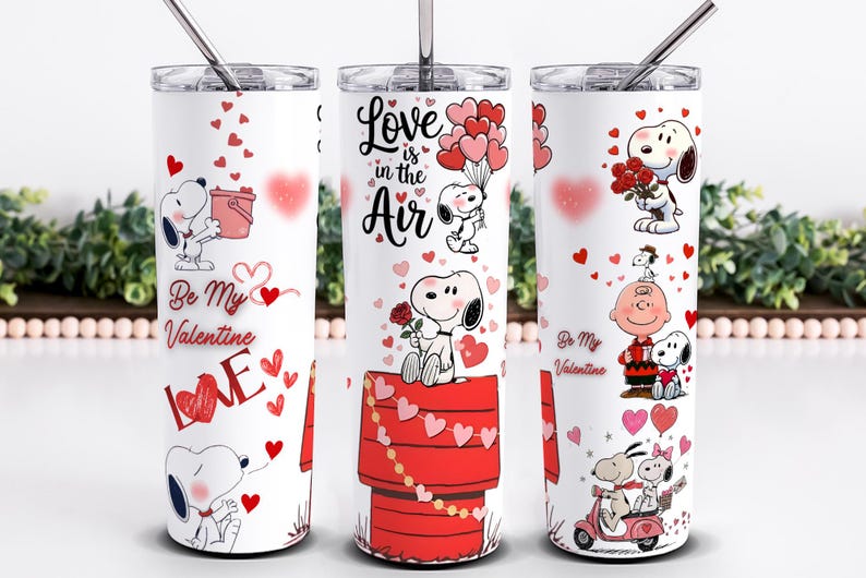 May include: White stainless steel tumbler featuring Snoopy and Woodstock Valentine's Day designs. The tumbler has a silver straw and lid. The designs include Snoopy with hearts, roses, and the text "Love is in the Air" and "Be My Valentine".