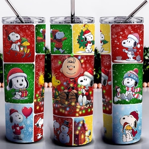 May include: A stainless steel tumbler featuring a festive design with Snoopy and Charlie Brown characters in a Christmas theme. The tumbler has a straw and a lid, and the design includes red, green, and blue colors.