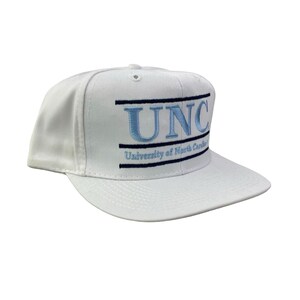 Puede incluir: Gorra de b&eacute;isbol blanca con visera plana, con las letras "UNC" bordadas en azul claro, con un borde negro. Debajo, el texto "University of North Carolina" en negro. Un sombrero cl&aacute;sico e informal.