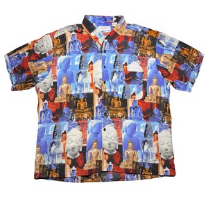 May include: Short-sleeved button-down shirt with a collage pattern featuring Buddha statues in various colors. The shirt has a classic collar and a pocket. The background colors include blue, red, and brown.