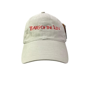 May include: A light beige baseball cap with the text "TEARS OF THE SUN" embroidered in red. The cap has a curved brim and a fabric strap closure. A tag is attached to the side.