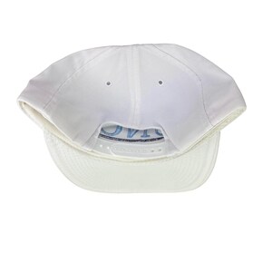 Puede incluir: Gorra de b&eacute;isbol blanca con visera curva y cierre trasero ajustable. La parte inferior de la visera es de un tono blanco m&aacute;s claro. La palabra "OVTA" est&aacute; bordada en azul claro en la parte trasera.